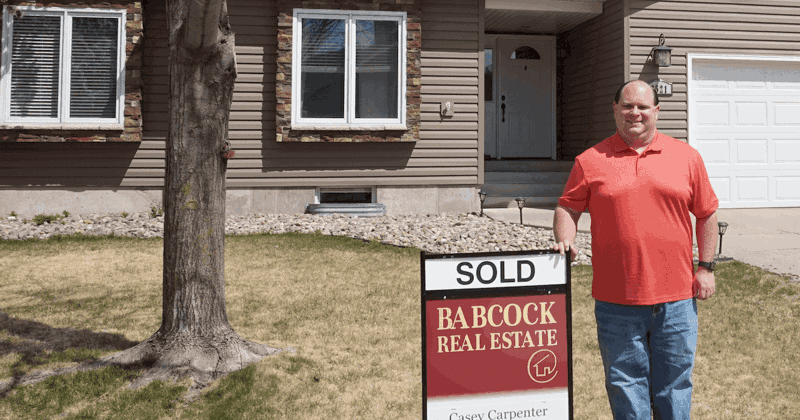 Casey in front of a house standing by a sold sign.