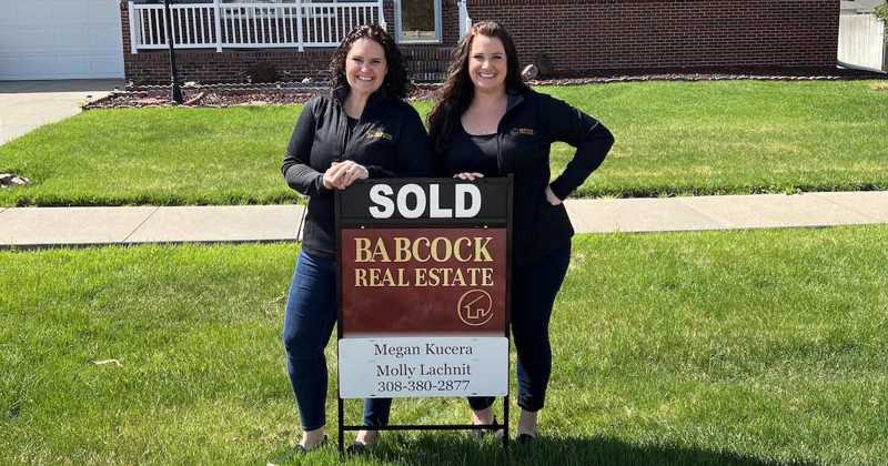Megan and Molly in front of a house standing by a sold sign.